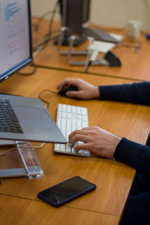 Young programmer typing on a freestanding white keyboard on a wooden table in front of two monitors