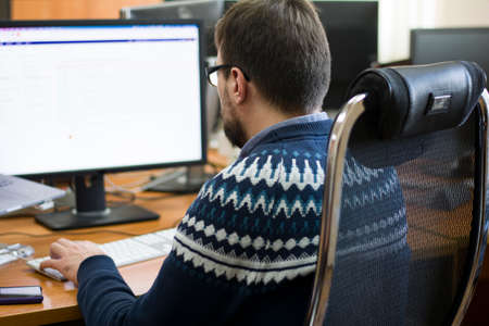 Young programmer typing on a freestanding white keyboard on a wooden table in front of two monitors