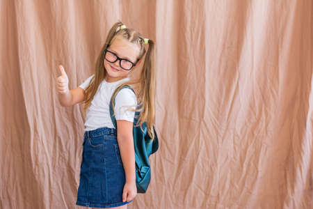 Portrait of a beautiful schoolgirl with a backpack who shows like in glasses in a white t-shirt and skirtの写真素材