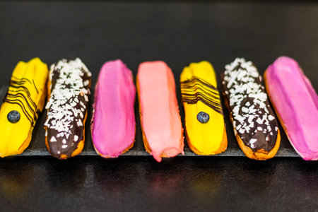 Close-up set of delicious eclairs with colorful dessert icing on black stone on table