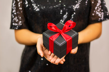 Closeup gift box wrapped in black paper with red ribbon in female handの写真素材