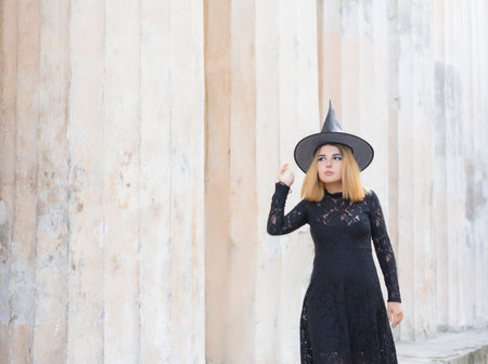 Happy gothic young woman in Halloween witch costume with hat on gray background