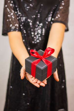 Female hands holding a black gift wrapped with red ribbon New Year and Merry Christmasの写真素材