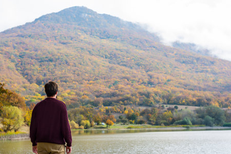 Back view man tourist in sweaters near the lake in the forest in autumn on natureの写真素材