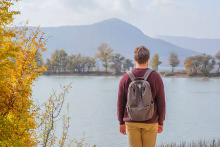Back view man tourist with backpack in sweaters near the lake in the forest in autumn on nature