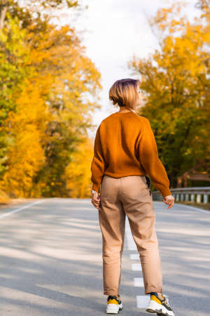 Faceless woman view from the back of a woman walking along the road in autumn in the forestの写真素材