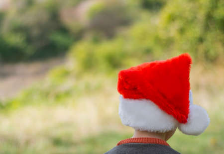 Back view boy wearing santa claus hat looking away outdoors background blurの写真素材