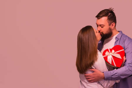 Young brunette woman kissing boyfriend in the room against pink background