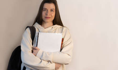 Student in trendy sweatshirts standing in hands holds notebooks on wall background with copy spaceの写真素材