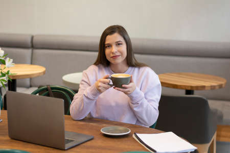 Woman drinking coffee or enjoys aromatic cappuccino in the morning in a cafe laptop mock upの写真素材