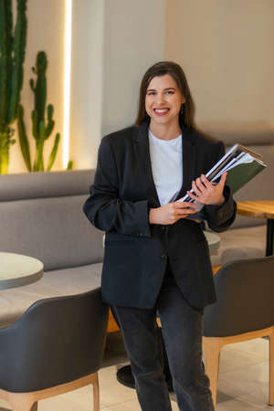 Happy smiling of confident businesswoman jacket holding laptop and a stack of papers of a cafeの写真素材