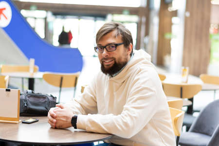 Smiling man in glasses with a beard in a beige sweatshirt mockup in everyday lifestyle in a cafeの写真素材