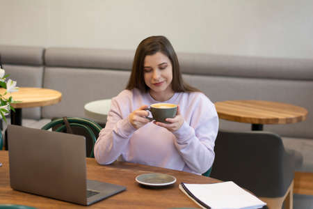 Woman hand holding with foam froth art in gray ceramic cup drinking coffee in a cafeの写真素材