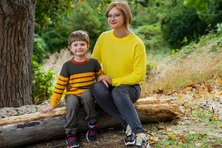 Adult smiling mother and cute son have a picnic in nature in the forest on an autumn dayの写真素材