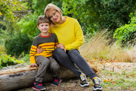 Young smiling mother hugging her son while sitting in the forest having fun spending time togetherの写真素材