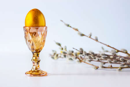 Easter golden egg in a golden egg holder with willow branches on a light backgroundの写真素材