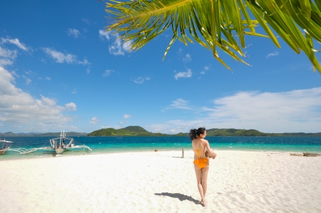 Portrait of single young bikini girl holds a coconut in her arm standing on white beachの写真素材