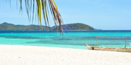 A banca  a type of outrigger boat native to the Philippines  and palm tree leaf on white beach, the shallow water shows beautiful layers of colors   Shot on Malcapuya Island, Coron, Palawan, Philippinesの写真素材