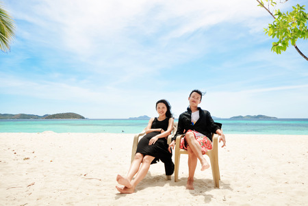 happy young couple sit on chair on beachの写真素材