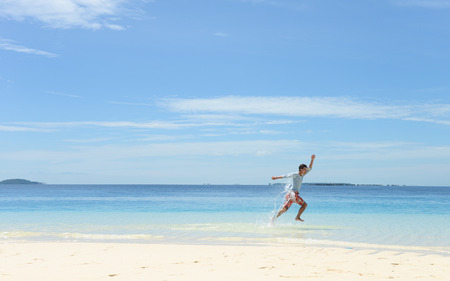 Side portrait of single young man running and jumping on tropical white sand beachの写真素材