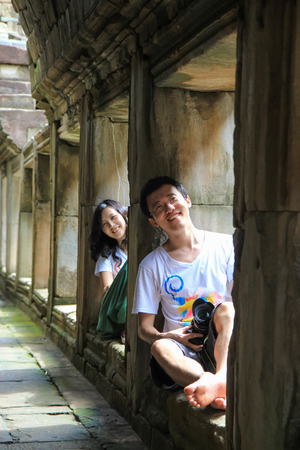young couple looking at camera  together, sitting on stone window in ancient passage, at Angkor Wat, Cambodiaの写真素材