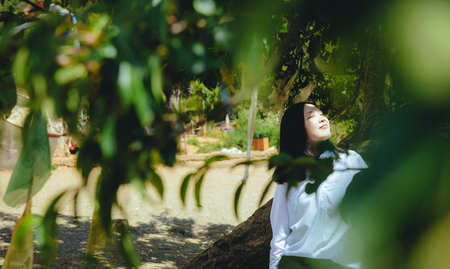 Single young Chinese woman leaning on tree trunk, smiling, on the bank of Lugu lake, Lijiang, Chinaの写真素材