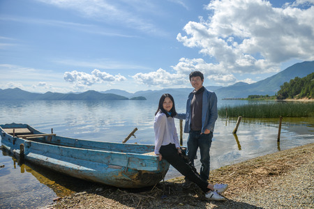 Young Asian couple looking at camera on lake bank, shot at Lugu Lake, Lijiang, Yunnan, Chinaの写真素材