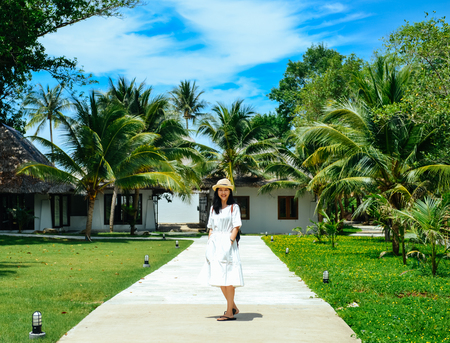 single Asian girl smiles happily standing in front of white villas and tropical garden, enjoying her vacation in resort at Ao Nang, Krabi, Thailand.の写真素材