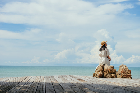 single Asian girl looks aside sitting on rock at tropical resort, Ao Nang, Krabi, Thailand.の写真素材