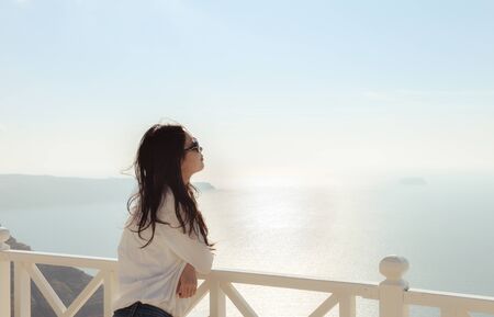 beautiful young girl on cliff balcony with sun glasses looks at sea horizon, in a wine factory at Santorini, Greece.の写真素材