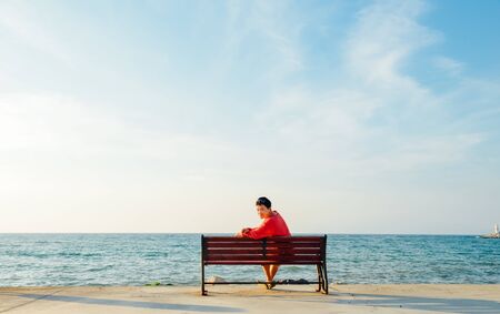 back portrait of young man looking back at camera on bench by the Aegean sea in Kusadasi, Turkeyの写真素材