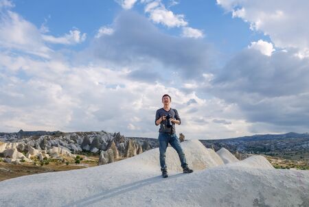 young man taking photo of landscape, standing on rocks in Goreme National Park, typical terrain landscape in Cappadocia, Turkeyの写真素材