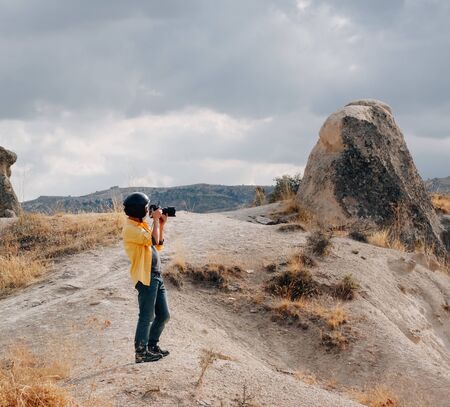 young man taking photo of landscape, standing on rocks in Goreme National Park, typical terrain landscape in Cappadocia, Turkeyの写真素材