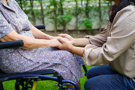 Caregiver help Asian elderly woman disability patient sitting on wheelchair in park, medical...