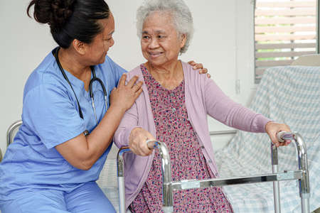 Doctor help Asian elderly woman disability patient walk with walker in nursing hospital, medical concept.の写真素材