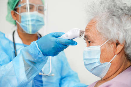 Doctor in ppe user infrared thermometer to check temperature of asian elderly woman patient for...