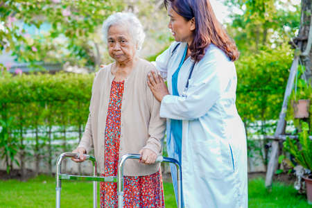 Doctor help Asian elderly woman disability patient walk with walker in park, medical concept.の写真素材