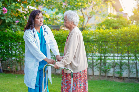 Doctor help Asian elderly woman disability patient walk with walker in park, medical concept.の写真素材
