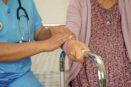 Caregiver help Asian elderly woman disability patient walk with walker in nursing hospital, medical concept.の写真素材