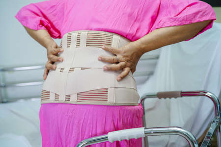 Asian senior pain back wearing elastic support belt with walker.の写真素材