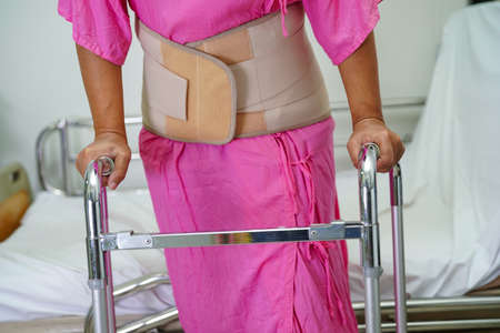 Asian senior pain back wearing elastic support belt with walker.の写真素材