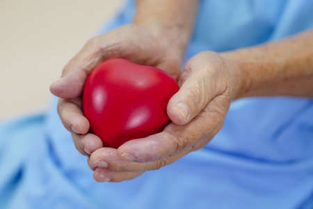 Asian elder senior woman patient holding red heart in hospital.