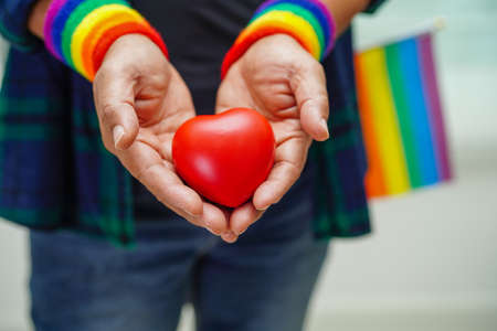 Asian woman holding red hert with rainbow flag, LGBT symbol rights and gender equality, LGBT Pride Month in June, LGBTQ, LGBTI, LGBTQA, LGBTQIAの写真素材