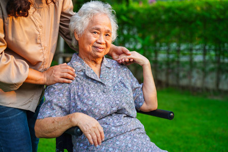 Caregiver help Asian elderly woman disability patient sitting on wheelchair in park, medical concept.の写真素材