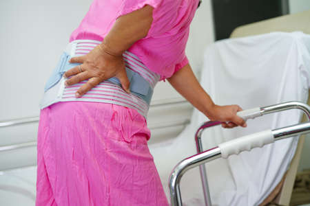 Asian senior pain back wearing elastic support belt with walker.の写真素材