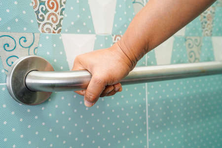 Asian woman patient use toilet support rail in bathroom, handrail safety grab bar, security in nursing hospital.の写真素材