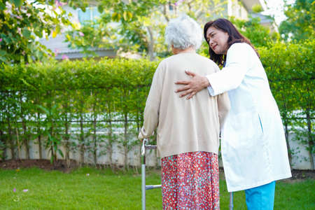Doctor help Asian elderly woman disability patient walk with walker in park, medical concept.の写真素材
