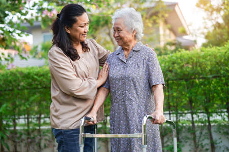 Caregiver help Asian elderly woman disability patient walk with walker in park, medical concept.の写真素材