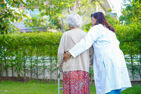 Doctor help Asian elderly woman disability patient walk with walker in park, medical concept.の写真素材