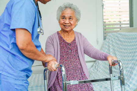 Doctor help Asian elderly woman disability patient walk with walker in nursing hospital, medical...